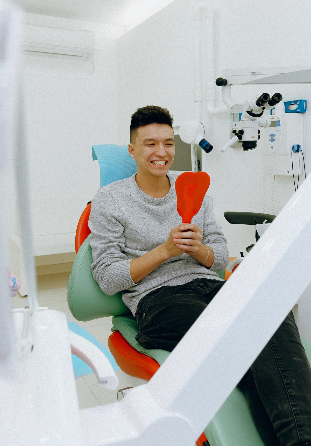Smiling patient in the dental chair admiring his new smile in a hand mirror at Sunset Dentistry